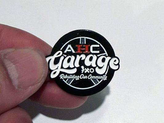 Close-up of AHC Garage enamel pin with glossy hard-enamel finish
